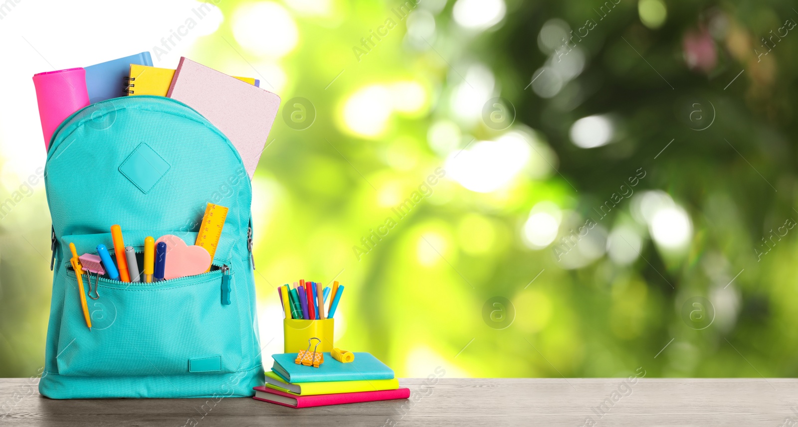 Image of Bright backpack with school stationery on table against blurred green background. Space for text