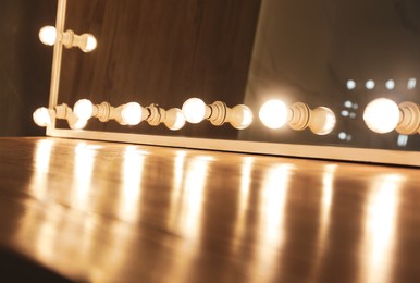 Photo of Modern mirror with light bulbs on wooden table, closeup