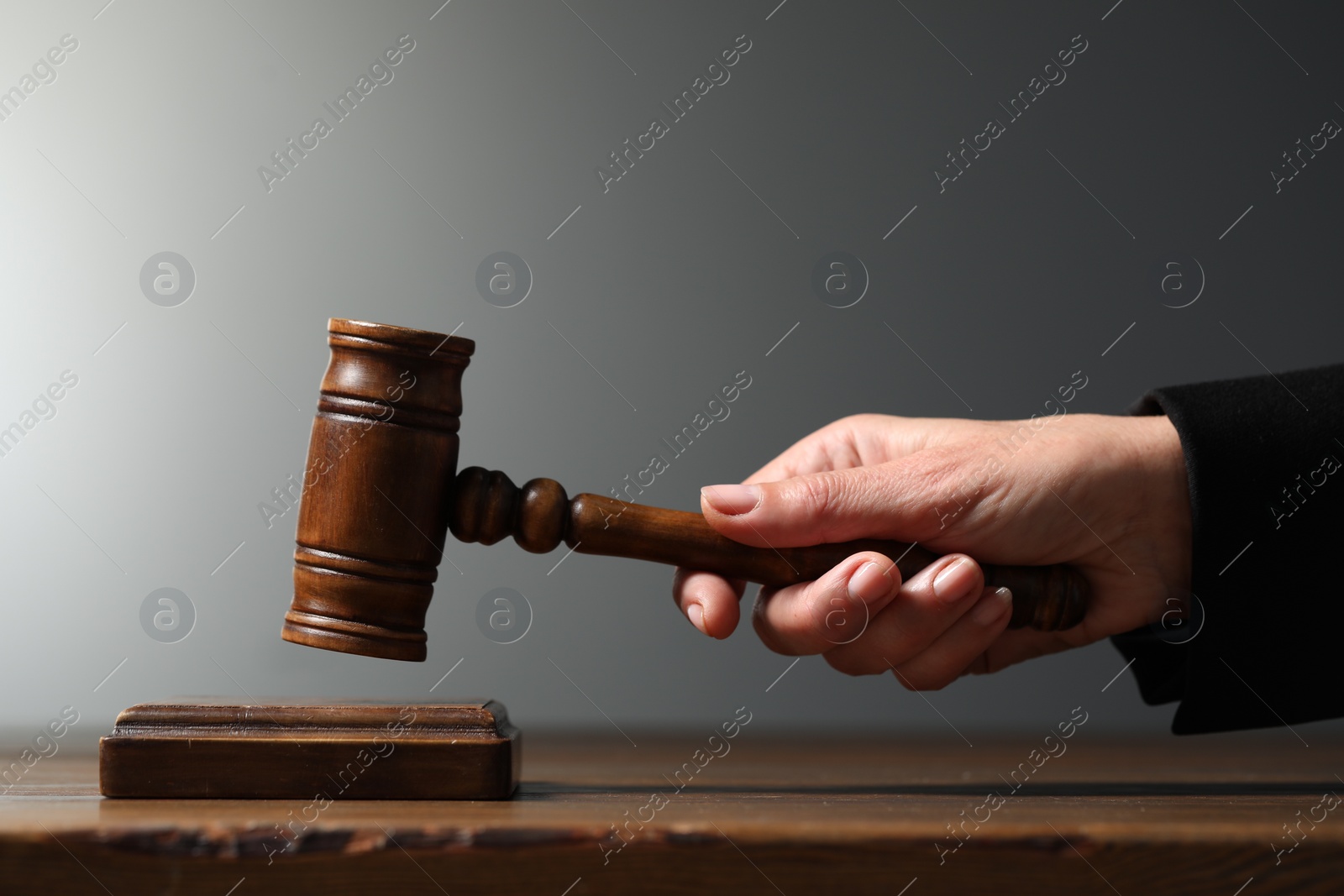 Photo of Judge striking mallet at wooden table against grey background, closeup
