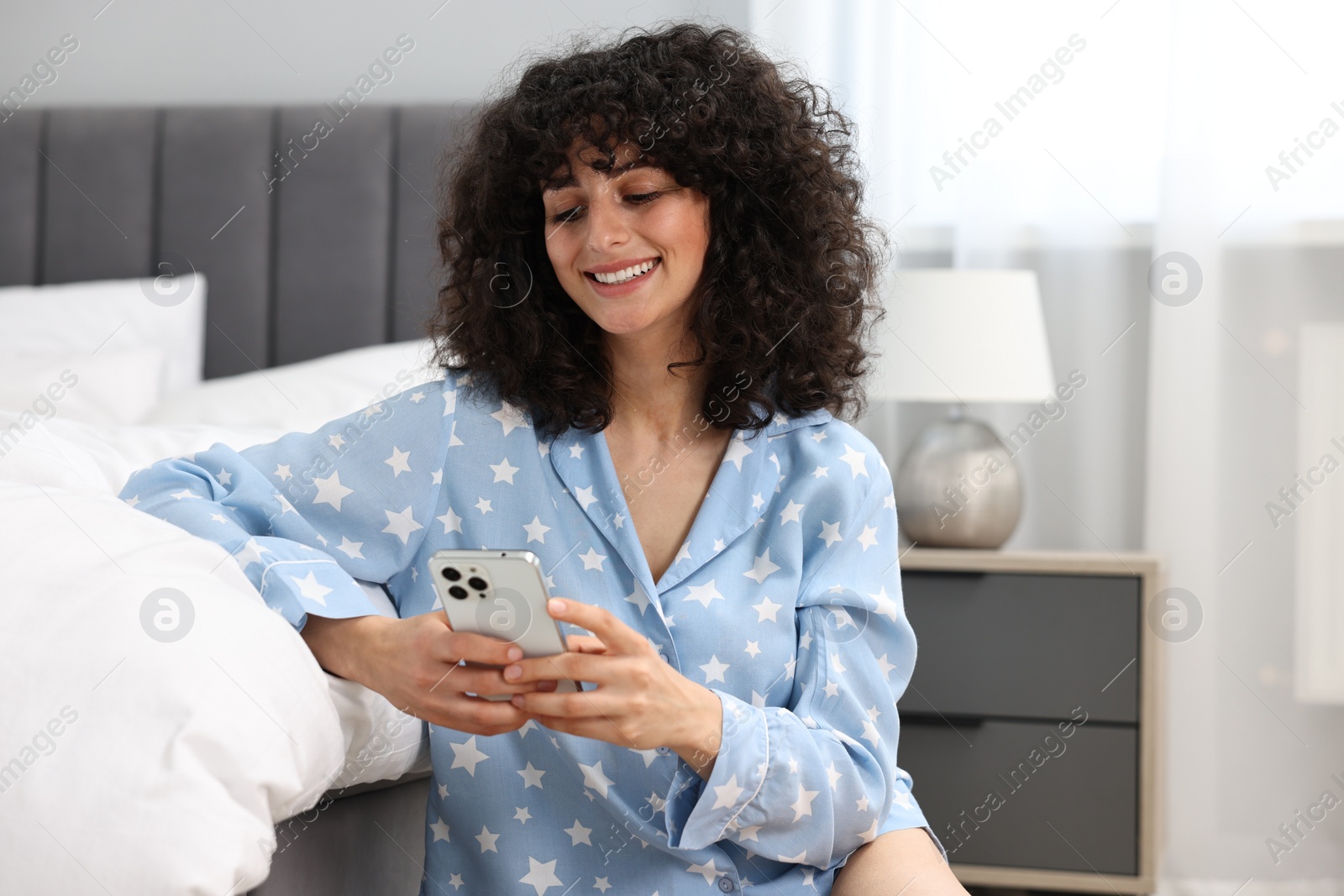 Photo of Beautiful young woman in stylish pyjama using smartphone at home