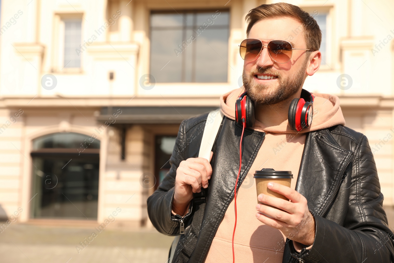 Photo of Happy young man with coffee on city street in morning