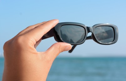 Photo of Woman holding stylish sunglasses near sea, closeup