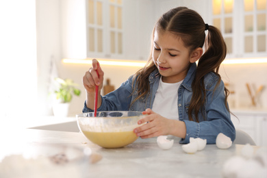 Photo of Cute little girl cooking dough at table in kitchen