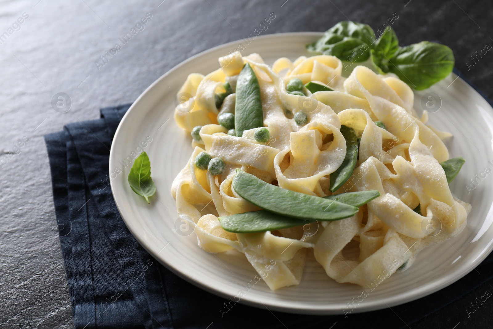 Photo of Delicious pasta with green peas and creamy sauce on black table