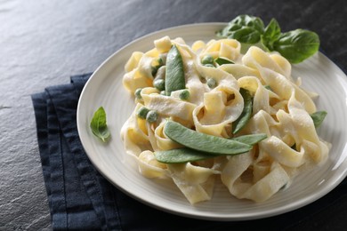 Photo of Delicious pasta with green peas and creamy sauce on black table