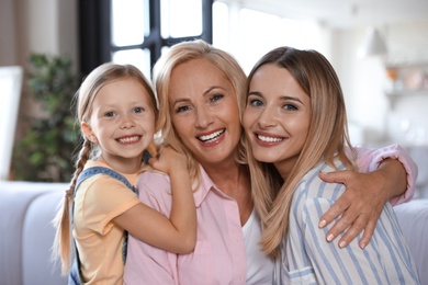 Photo of Young woman with mature mother and little daughter in living room