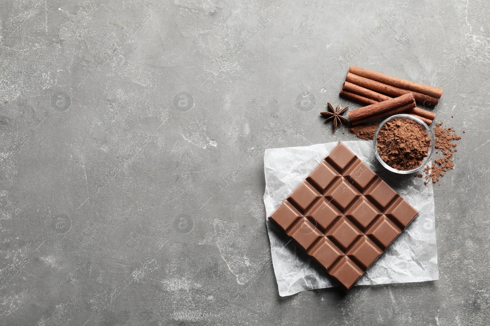 Photo of Chocolate bar and cocoa powder on grey background, flat lay. Space for text