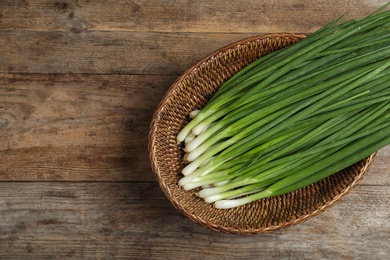 Photo of Wicker bowl with green onions on wooden table, top view Space for text