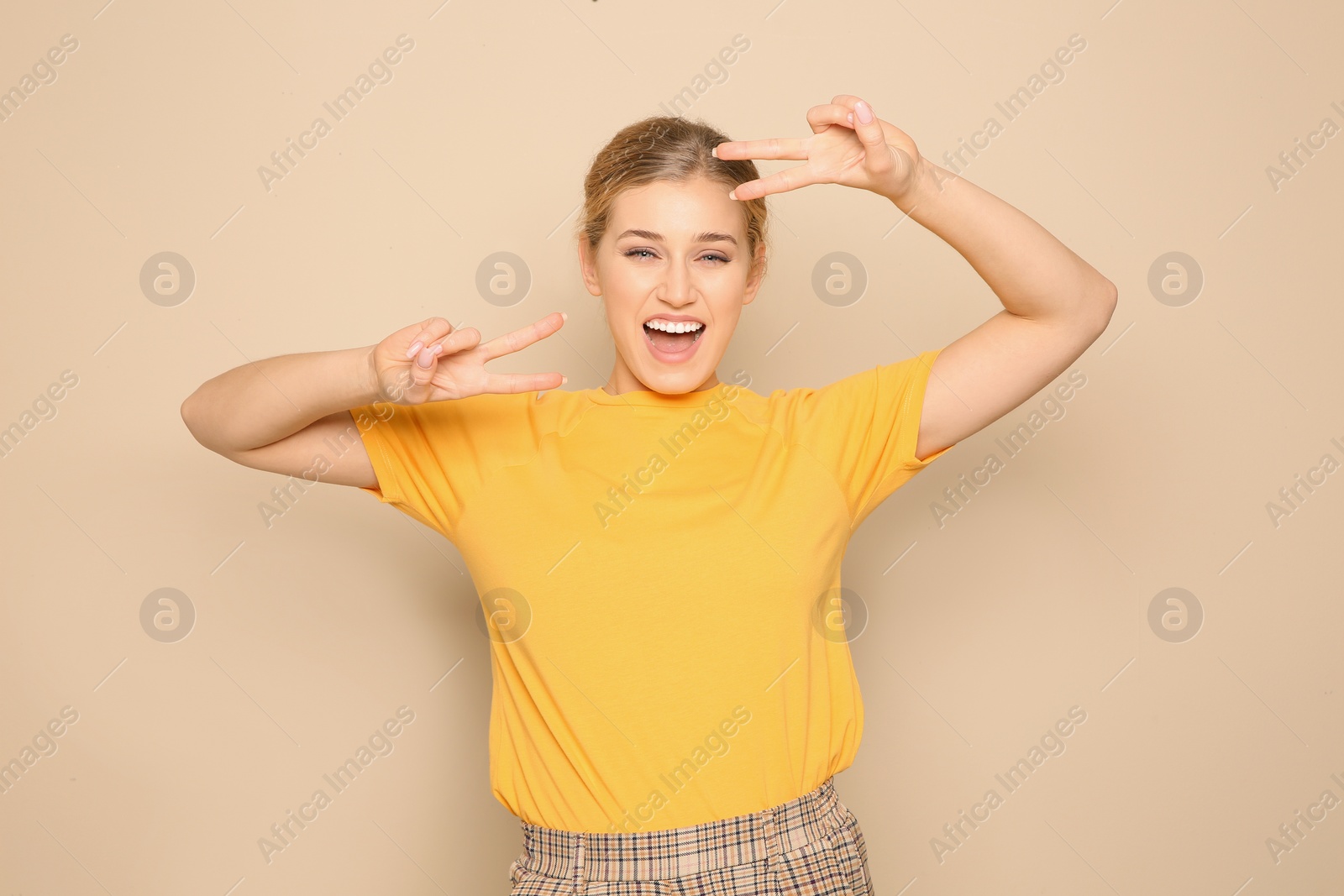 Photo of Happy young woman showing victory gesture on color background