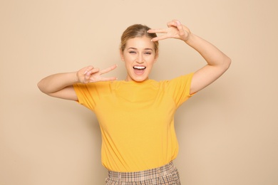 Happy young woman showing victory gesture on color background