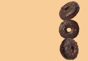 Image of Tasty chocolate donuts on moccasin color background, space for text