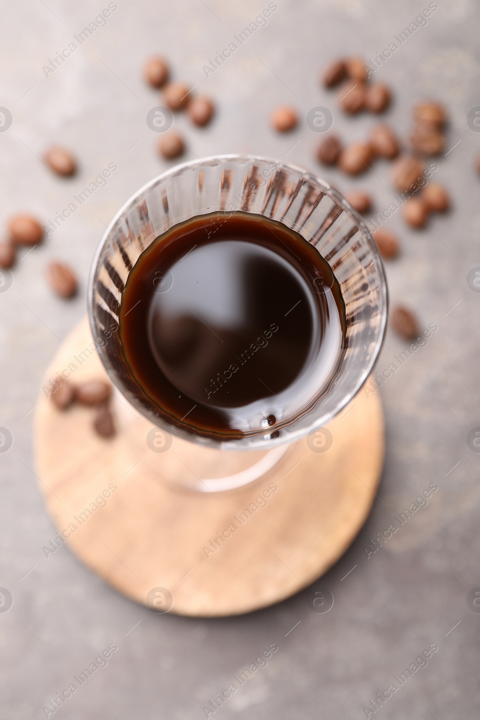 Photo of Shot glass with coffee liqueur and beans on light grey table, top view