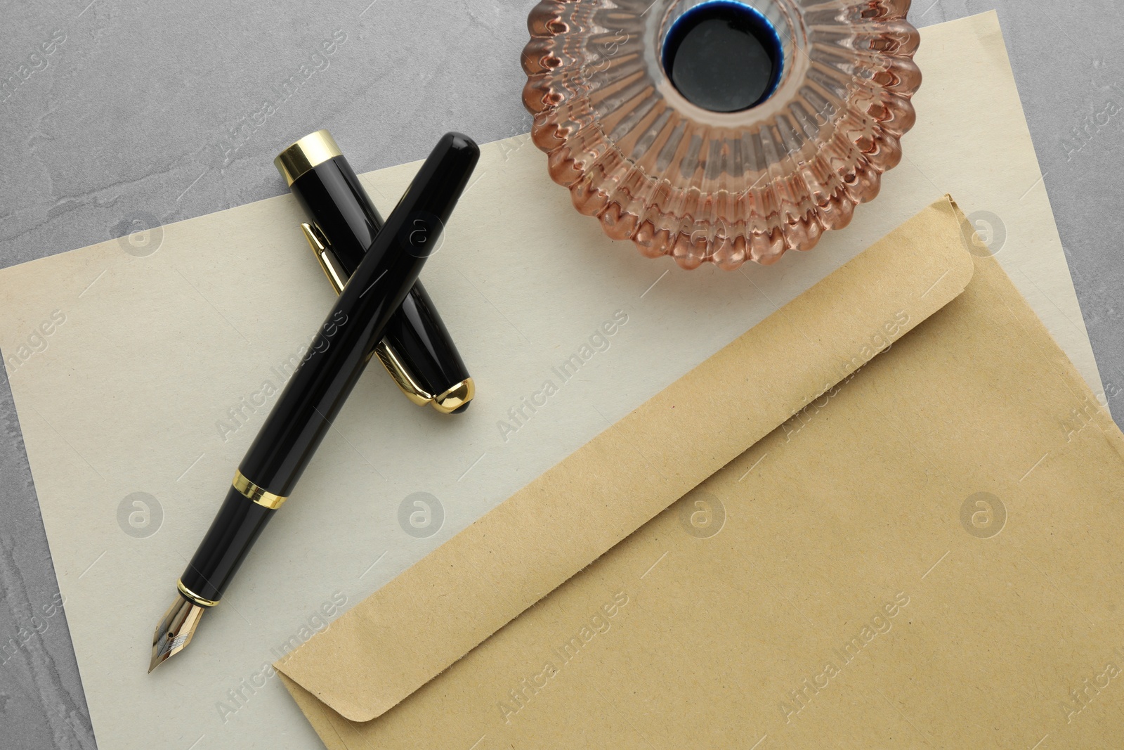 Photo of Stylish fountain pen, inkwell, envelope and paper on grey textured table, flat lay