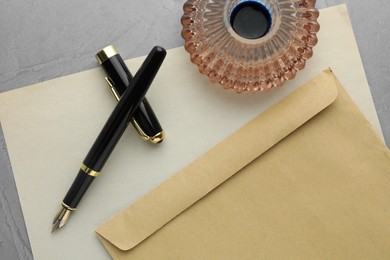 Photo of Stylish fountain pen, inkwell, envelope and paper on grey textured table, flat lay