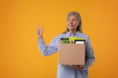 Photo of Happy unemployed senior woman with box of personal office belongings on orange background. Space for text