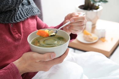 Sick young man eating broth to cure cold in bed at home