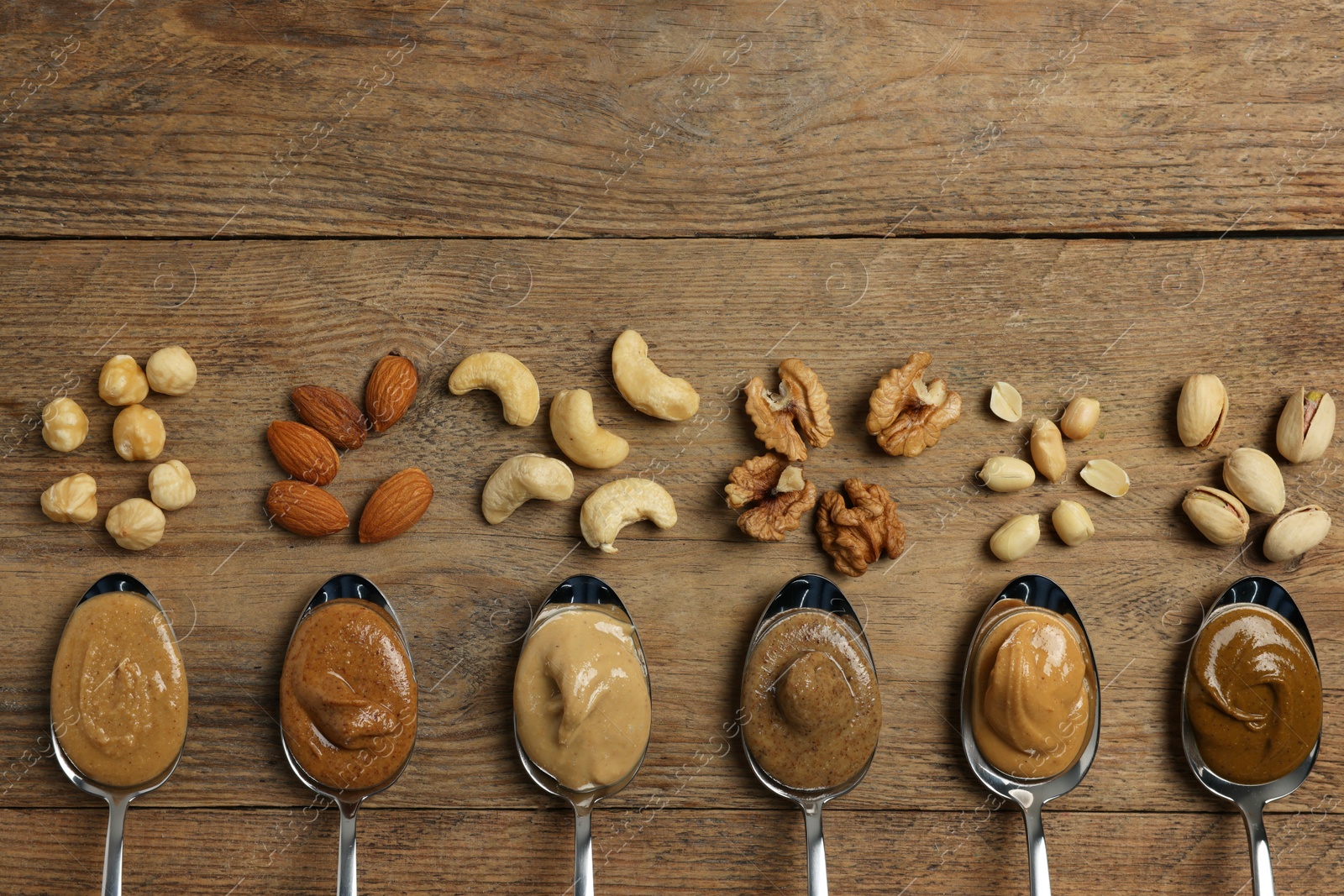 Photo of Tasty nut butters in spoons and raw nuts on wooden table, flat lay. Space for text