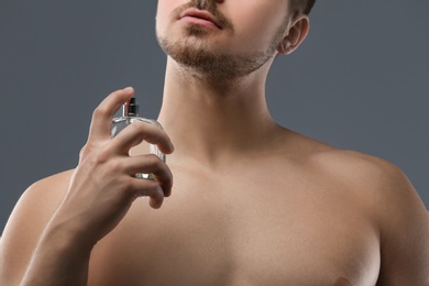 Photo of Handsome man using perfume on grey background, closeup