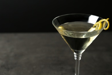 Glass of lemon drop martini cocktail with zest on stone table against black background, closeup. Space for text