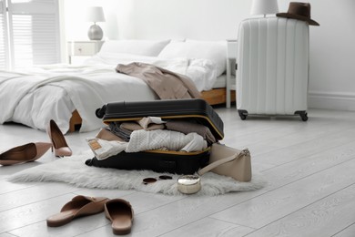 Photo of Open suitcase full of clothes, shoes and fashionable accessories on floor in bedroom. Space for text