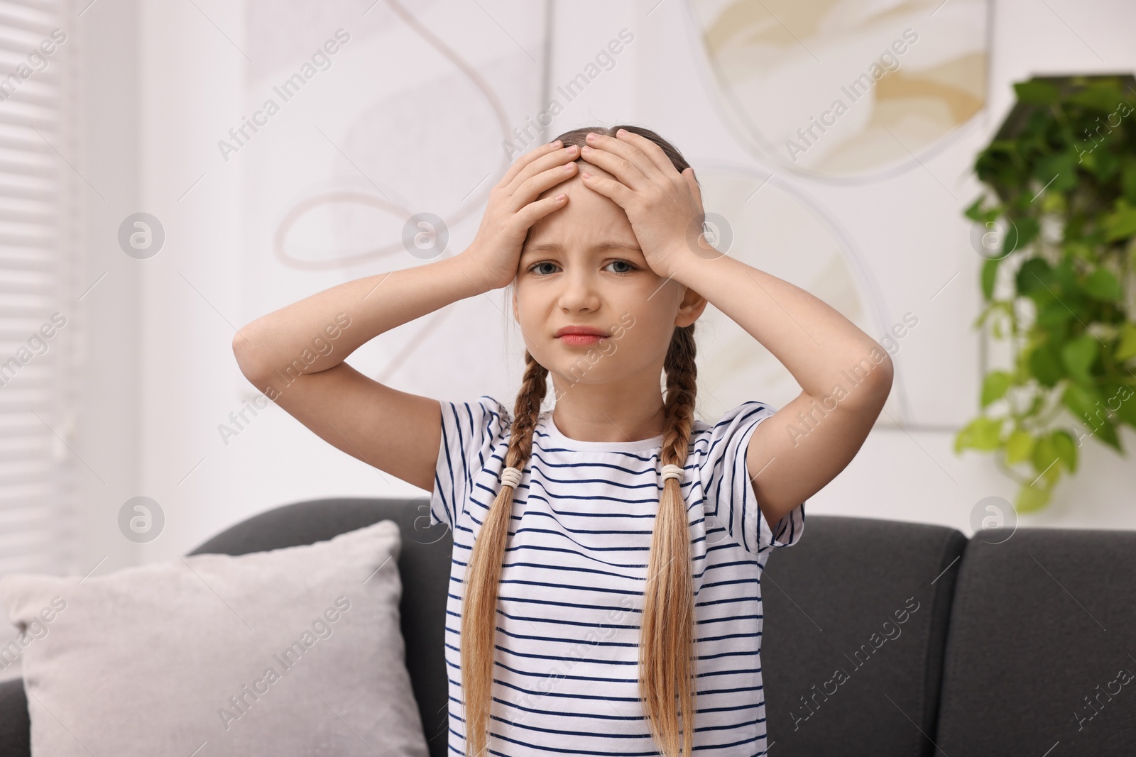 Photo of Little girl suffering from headache on sofa indoors