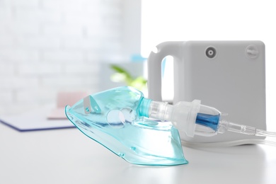 Photo of Modern nebulizer with face mask on white table indoors. Equipment for inhalation