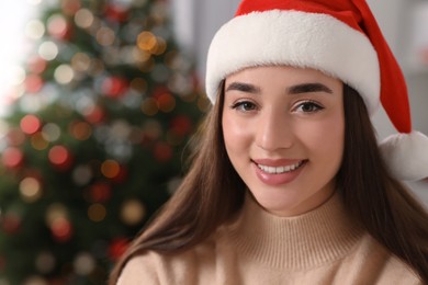 Photo of Portrait of smiling woman wearing red Christmas hat indoors. Space for text