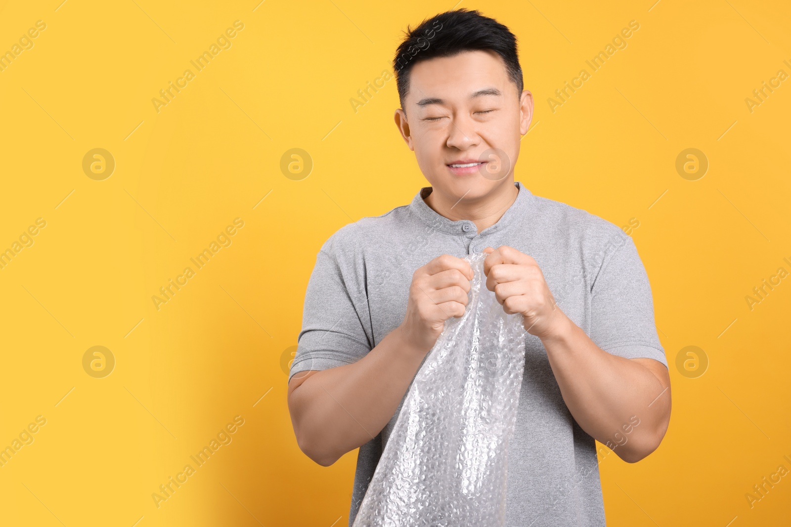 Photo of Asian man with bubble wrap on orange background. Space for text