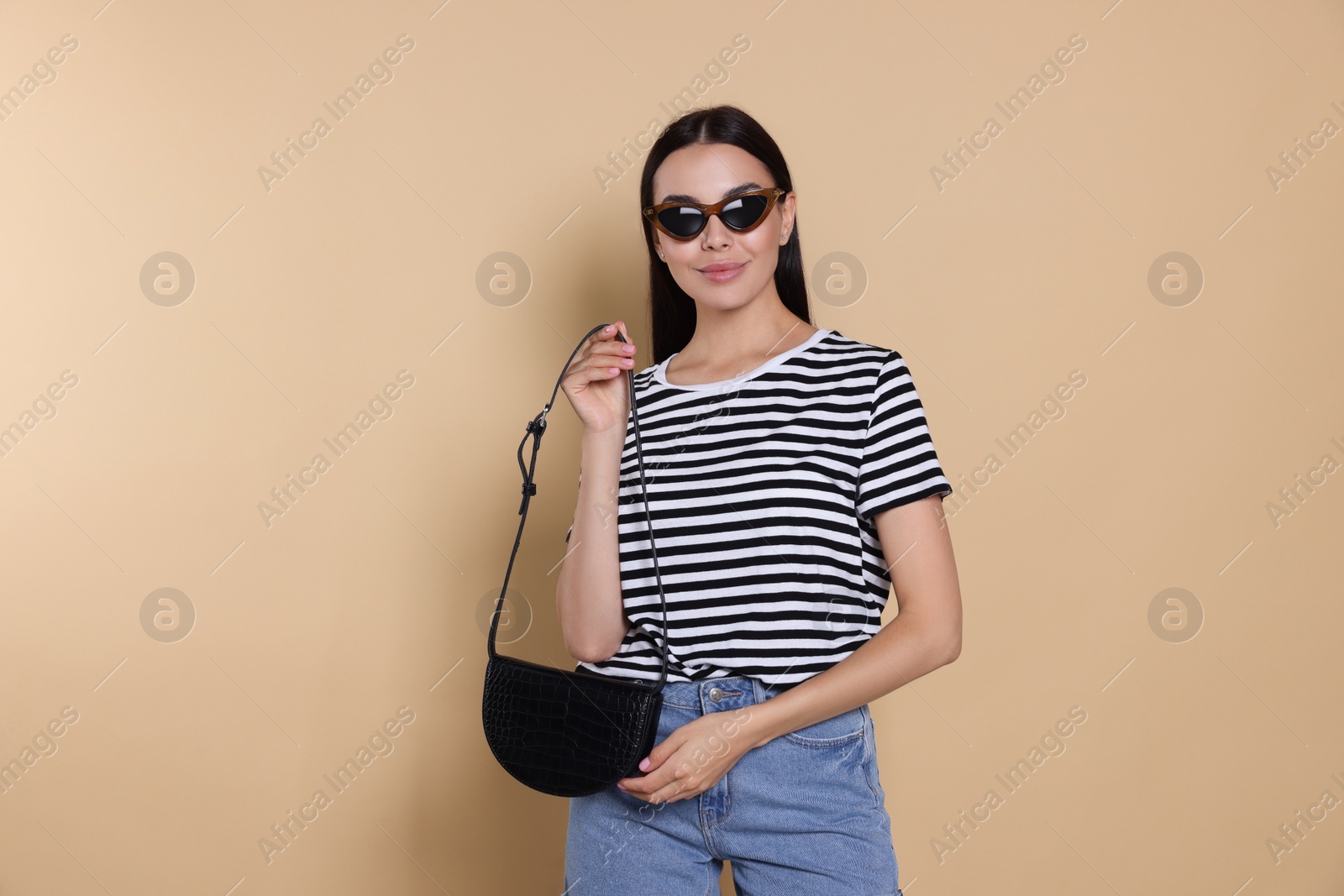 Photo of Beautiful young woman with stylish bag in sunglasses on beige background