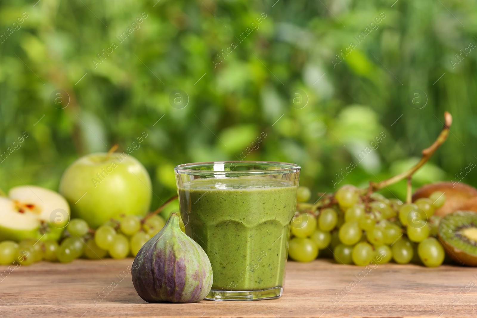 Photo of Glass of fresh green smoothie and ingredients on wooden table outdoors, space for text