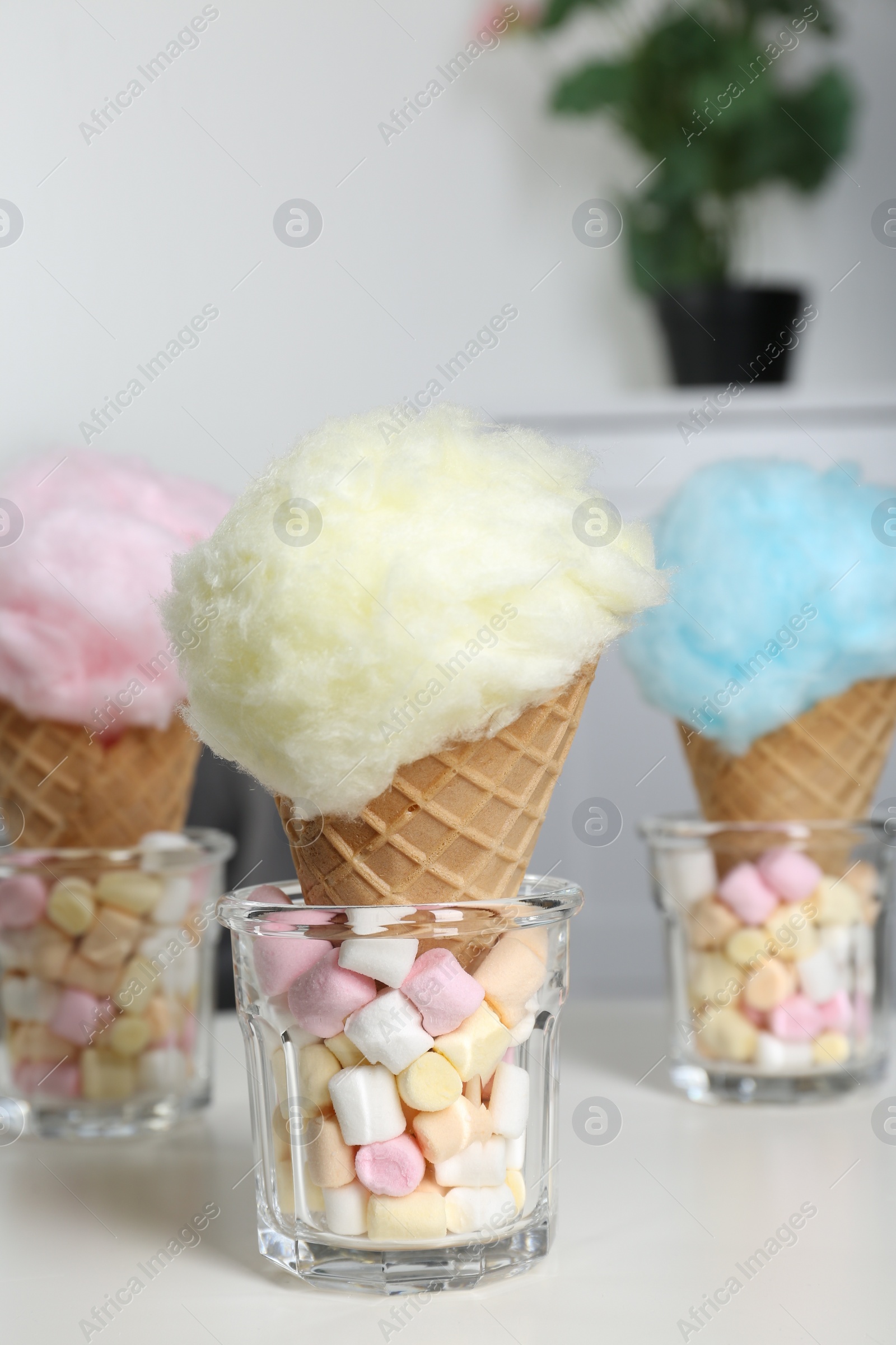 Photo of Sweet cotton candies in waffle cones and marshmallows on white table indoors, closeup