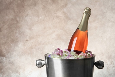 Photo of Bottle of champagne with floral ice cubes in bucket on color background. Space for text