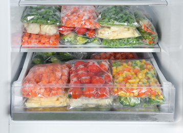 Plastic bags with different frozen vegetables in refrigerator