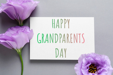 Beautiful Eustoma flowers and phrase HAPPY GRANDPARENTS DAY on gray background