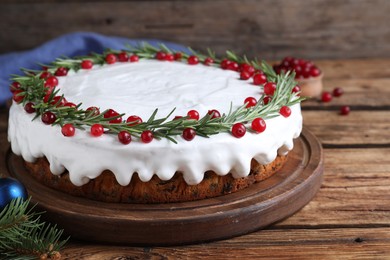Traditional Christmas cake decorated with rosemary and cranberries on wooden table, closeup