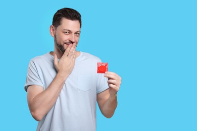 Photo of Confused man holding condom on light blue background. Space for text