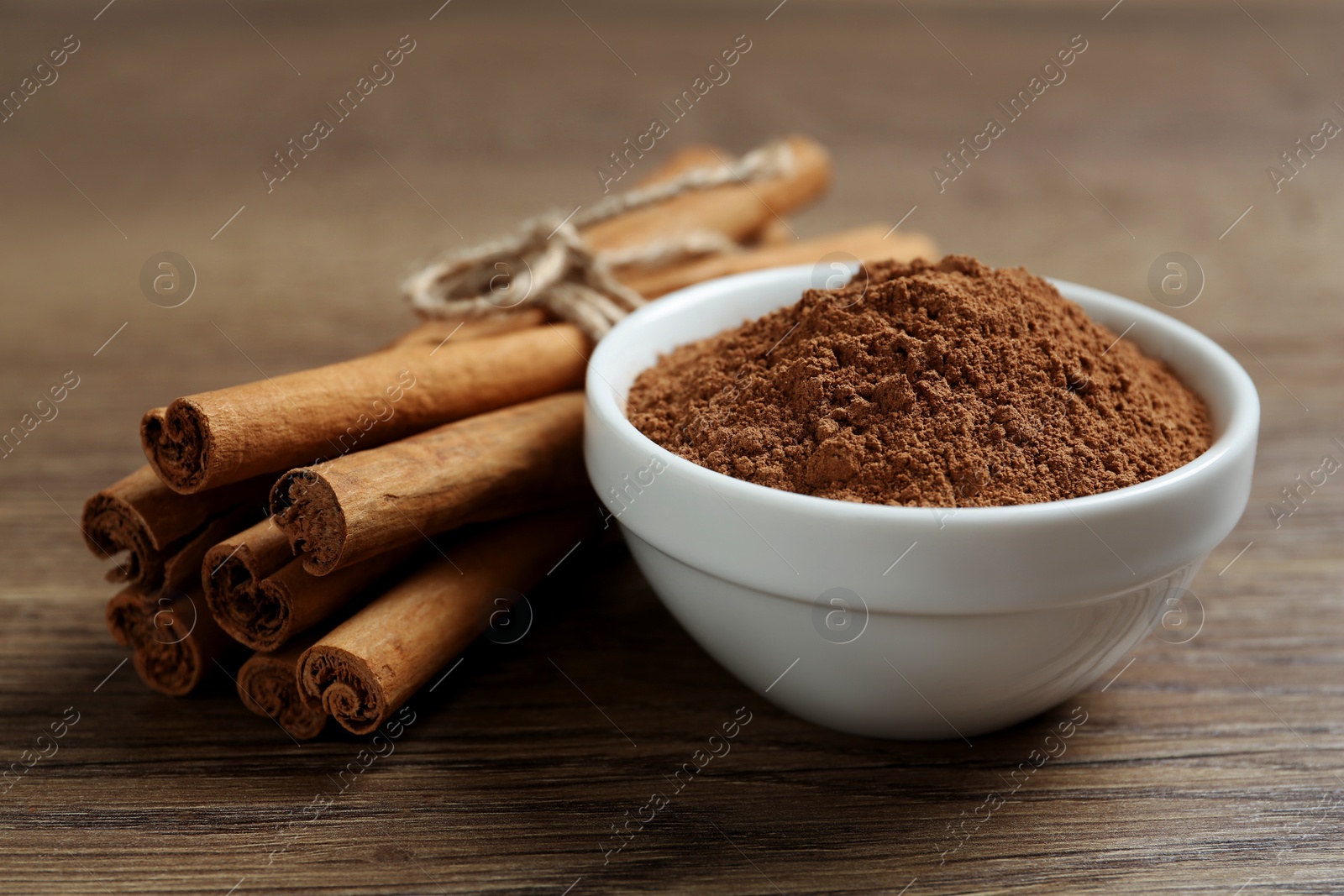 Photo of Cinnamon powder and sticks on wooden table, closeup