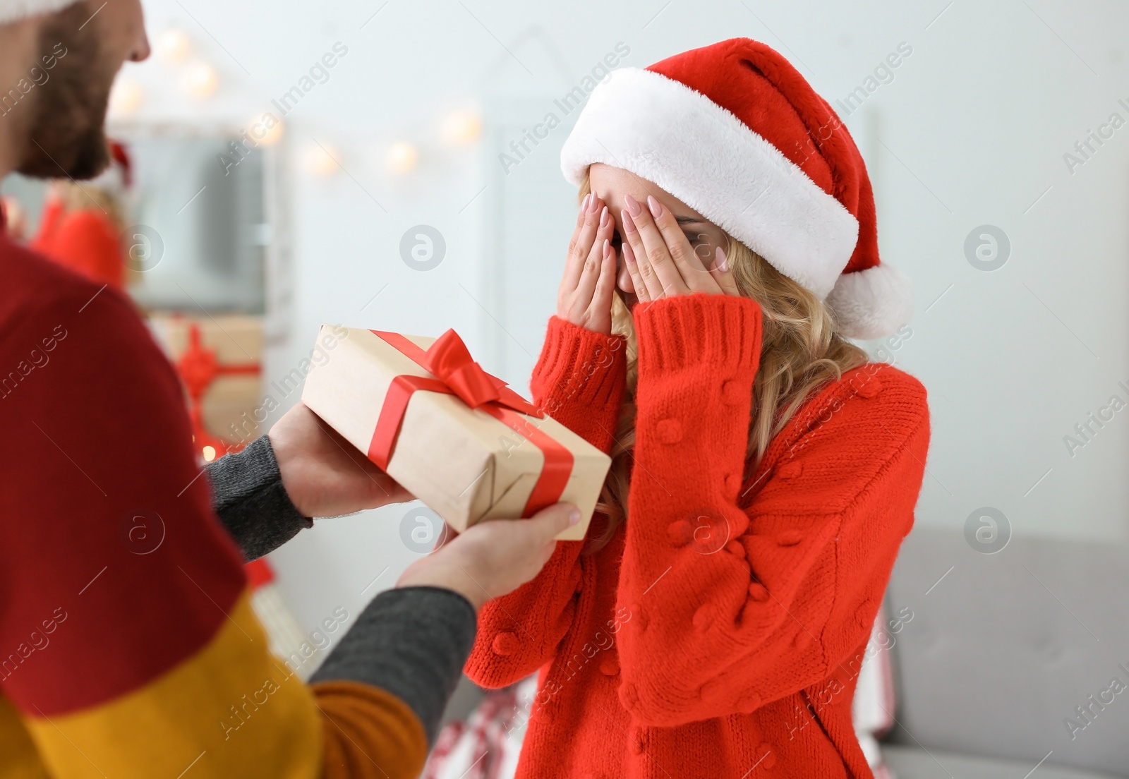 Photo of Young couple in Santa hats with Christmas gift at home