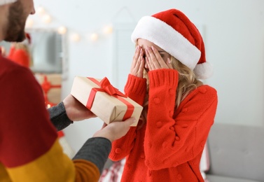 Photo of Young couple in Santa hats with Christmas gift at home