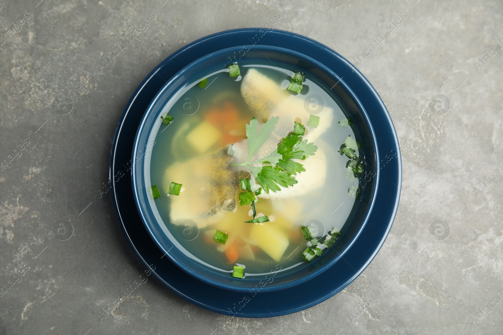 Photo of Delicious fish soup in bowl on grey table, top view