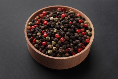 Photo of Wooden bowl of peppercorn mix on dark background