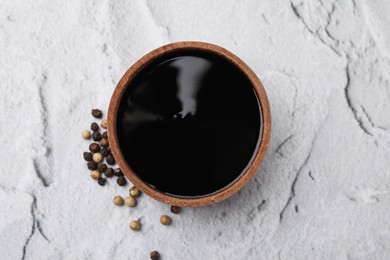 Photo of Wooden bowl with balsamic vinegar and peppercorns on white textured table, top view