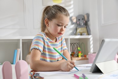 Photo of Little girl learning English with tablet indoors at online lesson