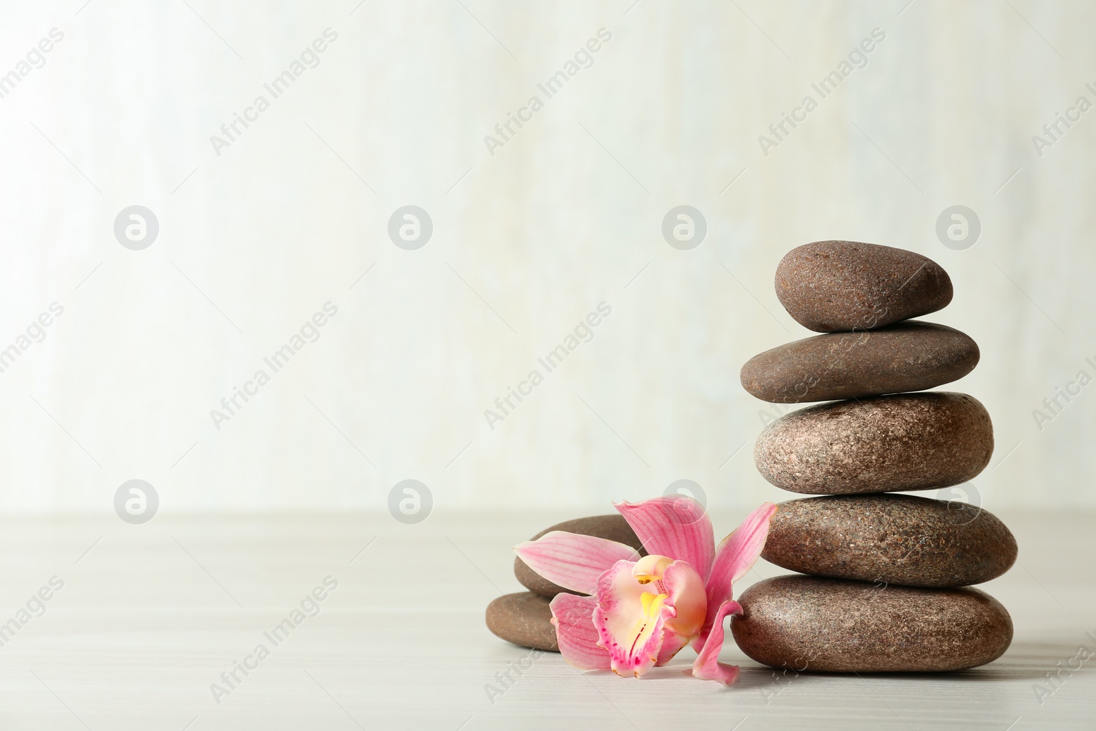 Photo of Stack of spa stones and flower on table against white background, space for text