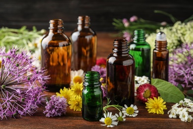 Photo of Different bottles of essential oils and flowers on table
