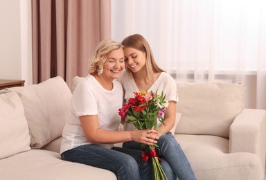 Photo of Young daughter congratulating her mom with flowers at home. Happy Mother's Day