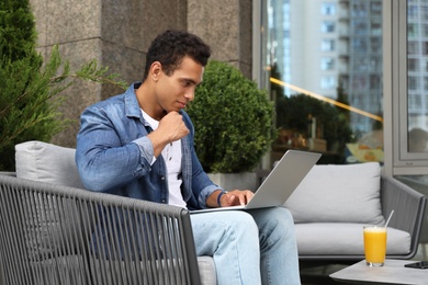 Photo of Portrait of handsome young African-American man with laptop in outdoor cafe