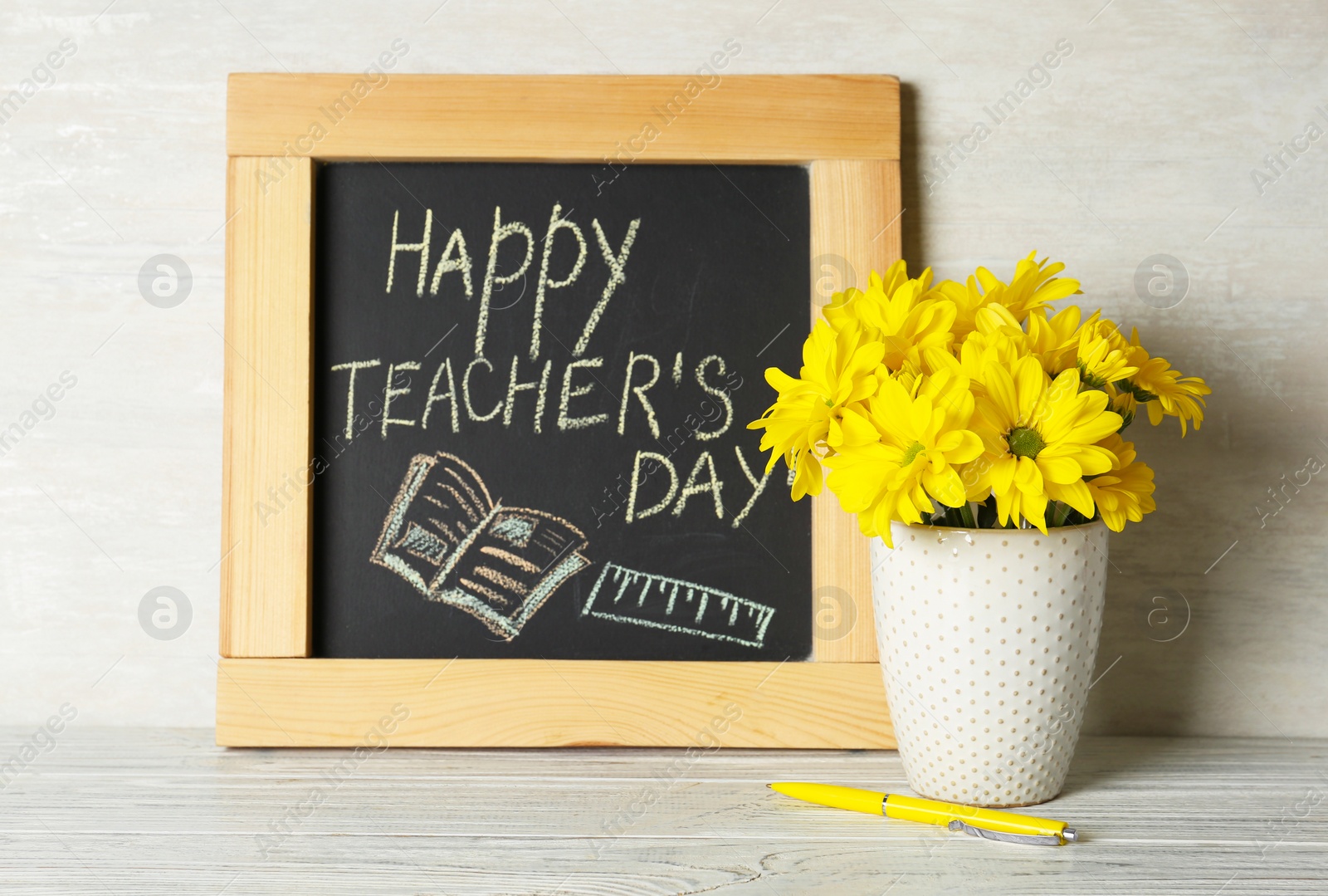 Photo of Chalkboard with inscription HAPPY TEACHER'S DAY and vase of flowers on wooden table against light wall