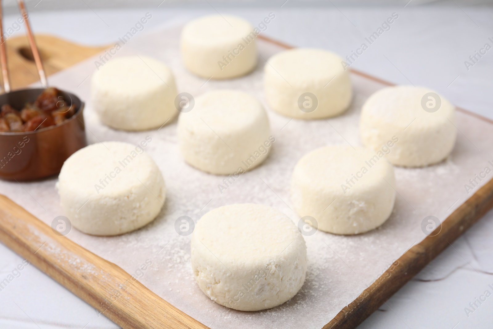 Photo of Uncooked cottage cheese pancakes and raisin on white table, closeup