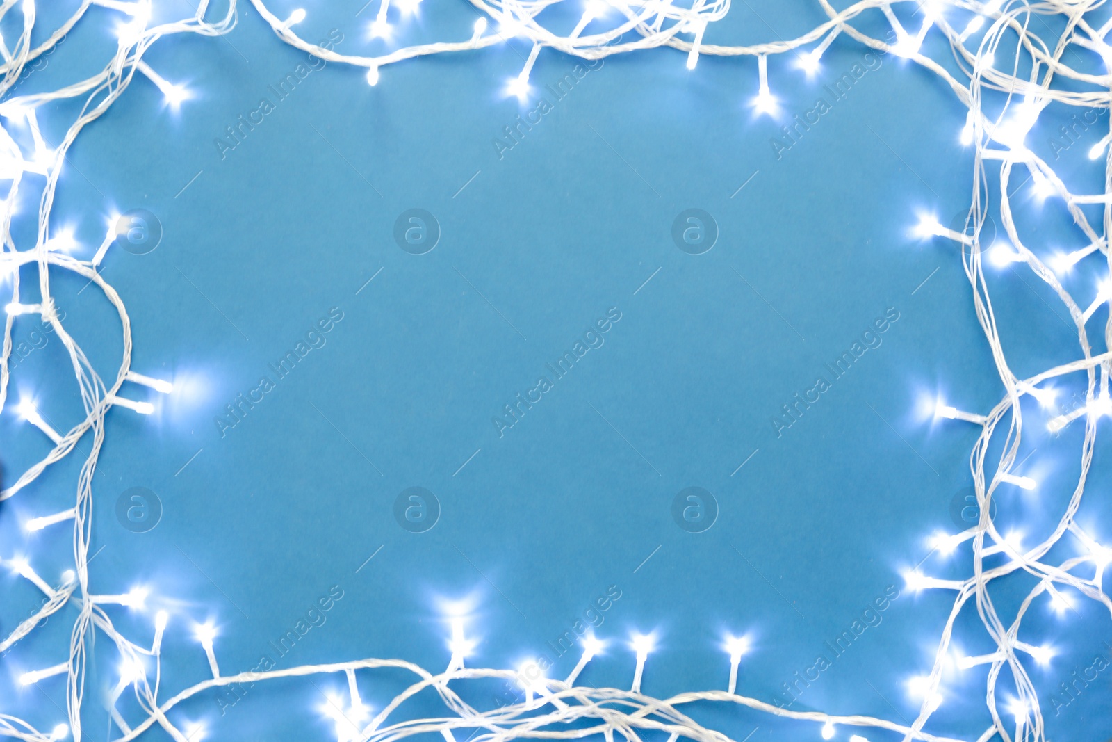 Photo of Frame made with Christmas lights on blue background, top view. Space for text